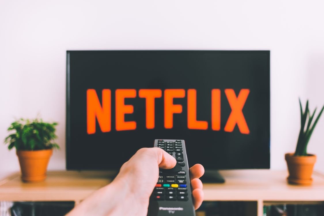 Persona sosteniendo un control remoto apuntando a una pantalla de streaming