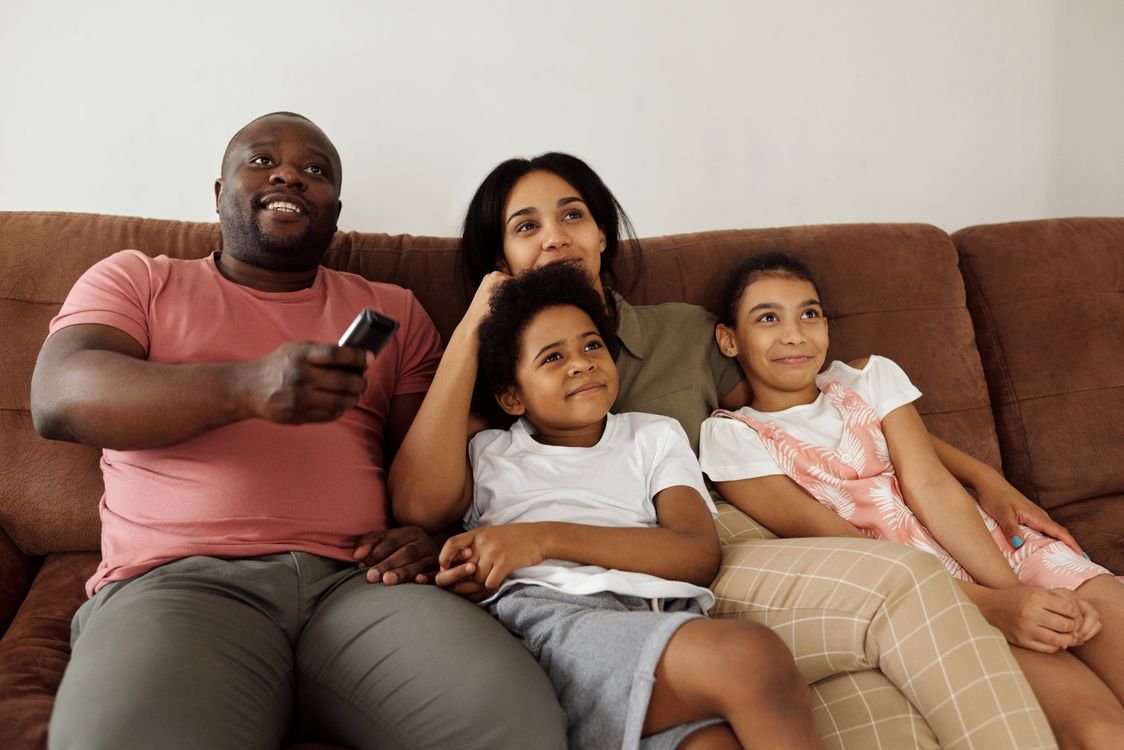 Familia sentada en el sofá viendo televisión juntos en la sala de estar